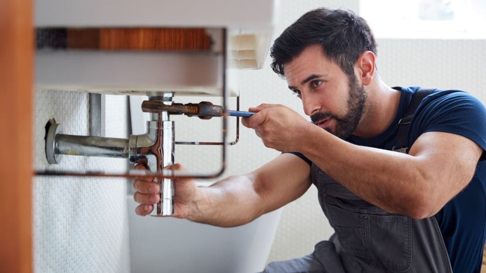 A New Zealand plumber in hi-vis working on the tap and pipes under a kitchen sink.